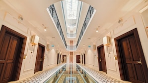 A grand hotel corridor with a glass floor, ornate doors, and a central skylight.