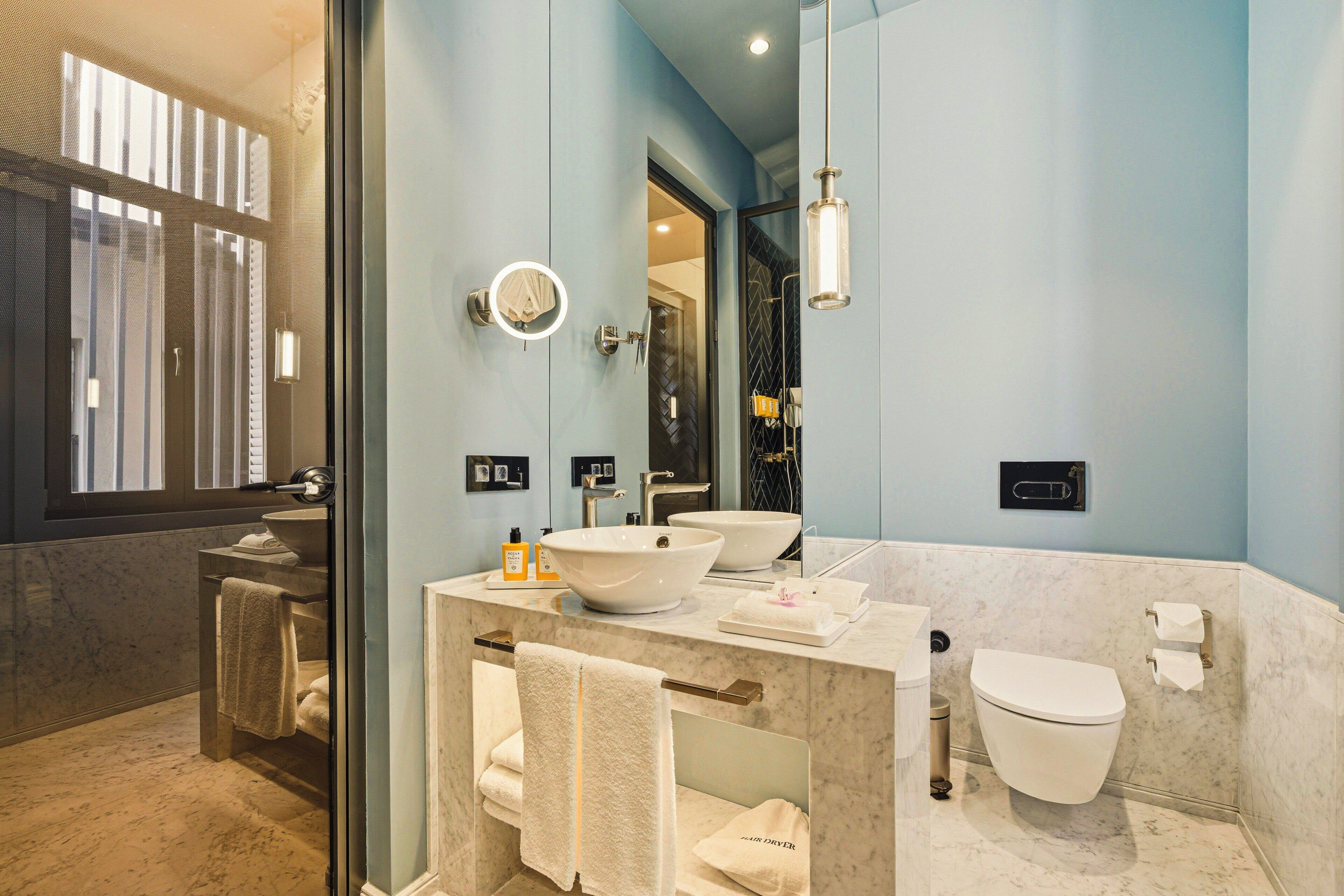 A modern bathroom with a large mirror, two sinks, a toilet, and a towel rack.
