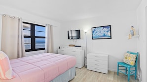 Una camera da letto con un letto, una cassettiera, una sedia, un televisore e una finestra con tende.