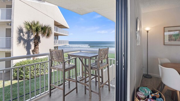 Un balcone con due sedie di legno e un tavolino, con vista su una spiaggia e l'oceano.