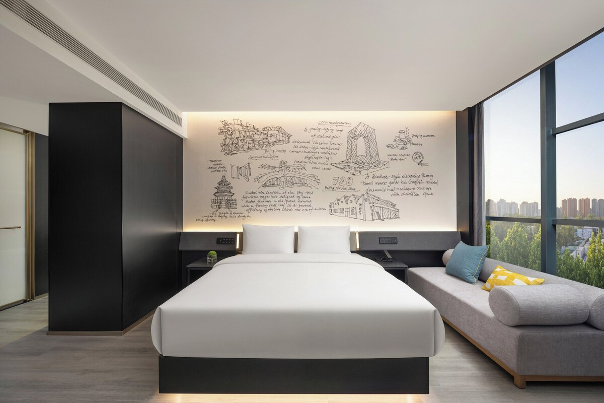 A modern hotel room with a large bed, a sofa, and a wall mural.