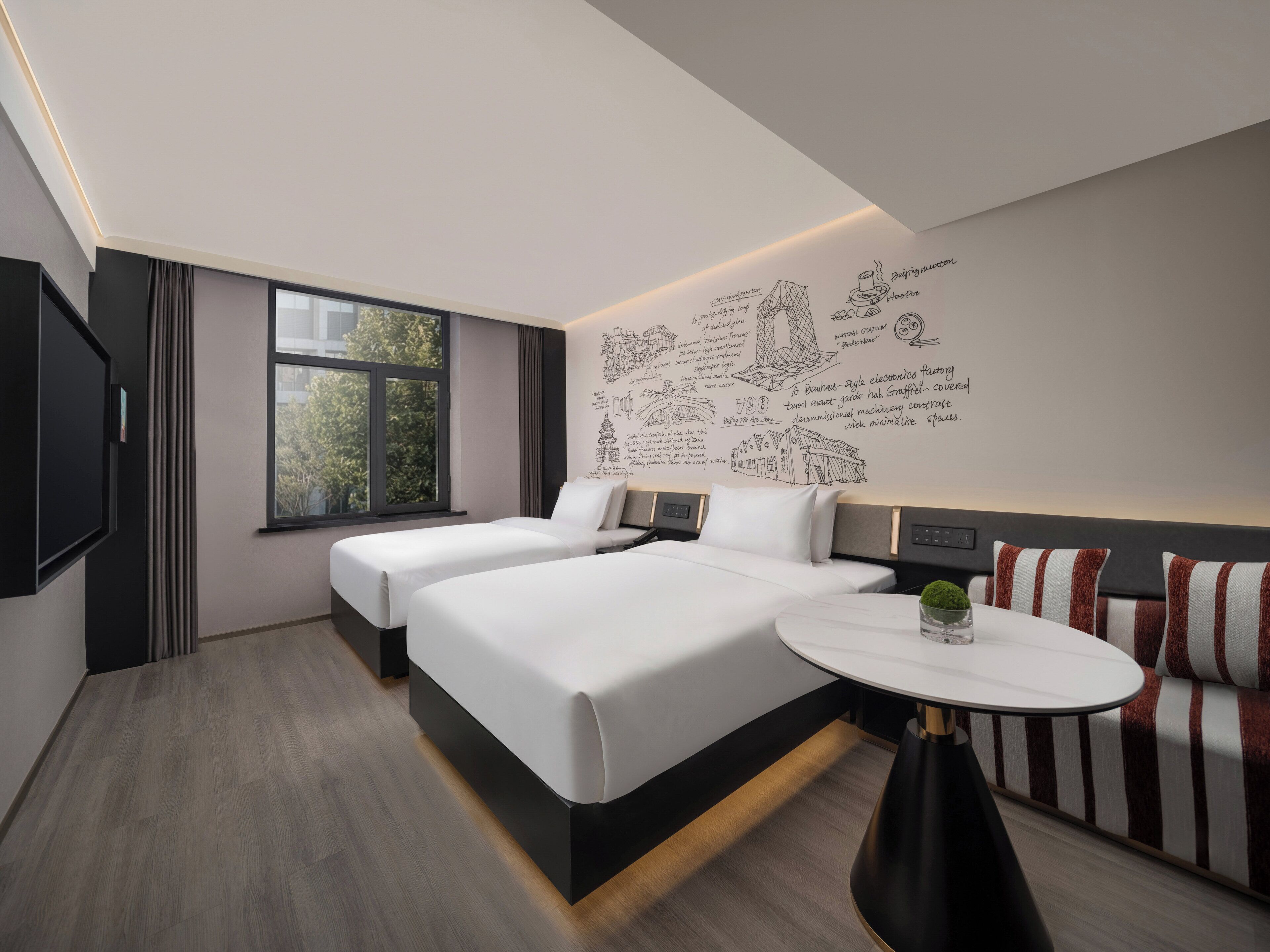 A modern hotel room with a large bed, a small round table, and a wall with artistic sketches.