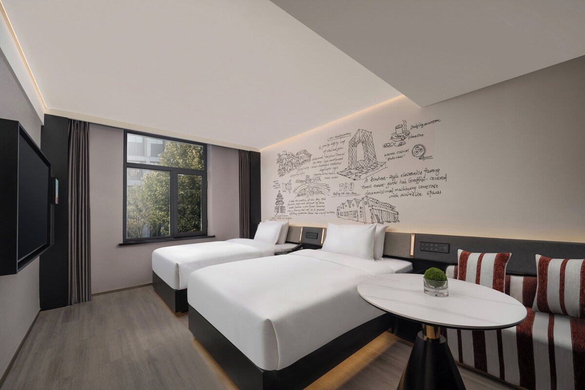 A modern hotel room with a large bed, a small round table, and a wall with artistic sketches.