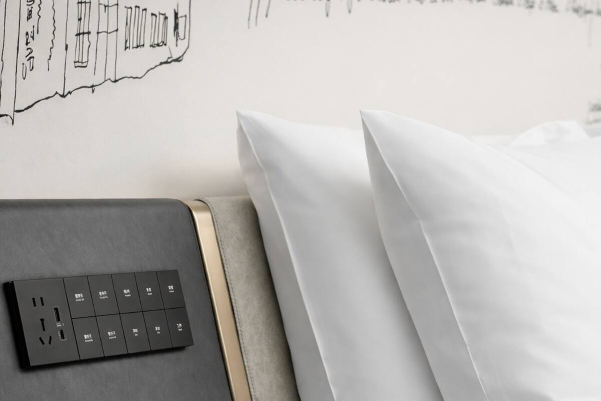 Ein modernes Bett mit weißer Bettwäsche, ein graues Kopfstück mit Bedienfeld und eine Wand mit einer einfachen Linienzeichnung.