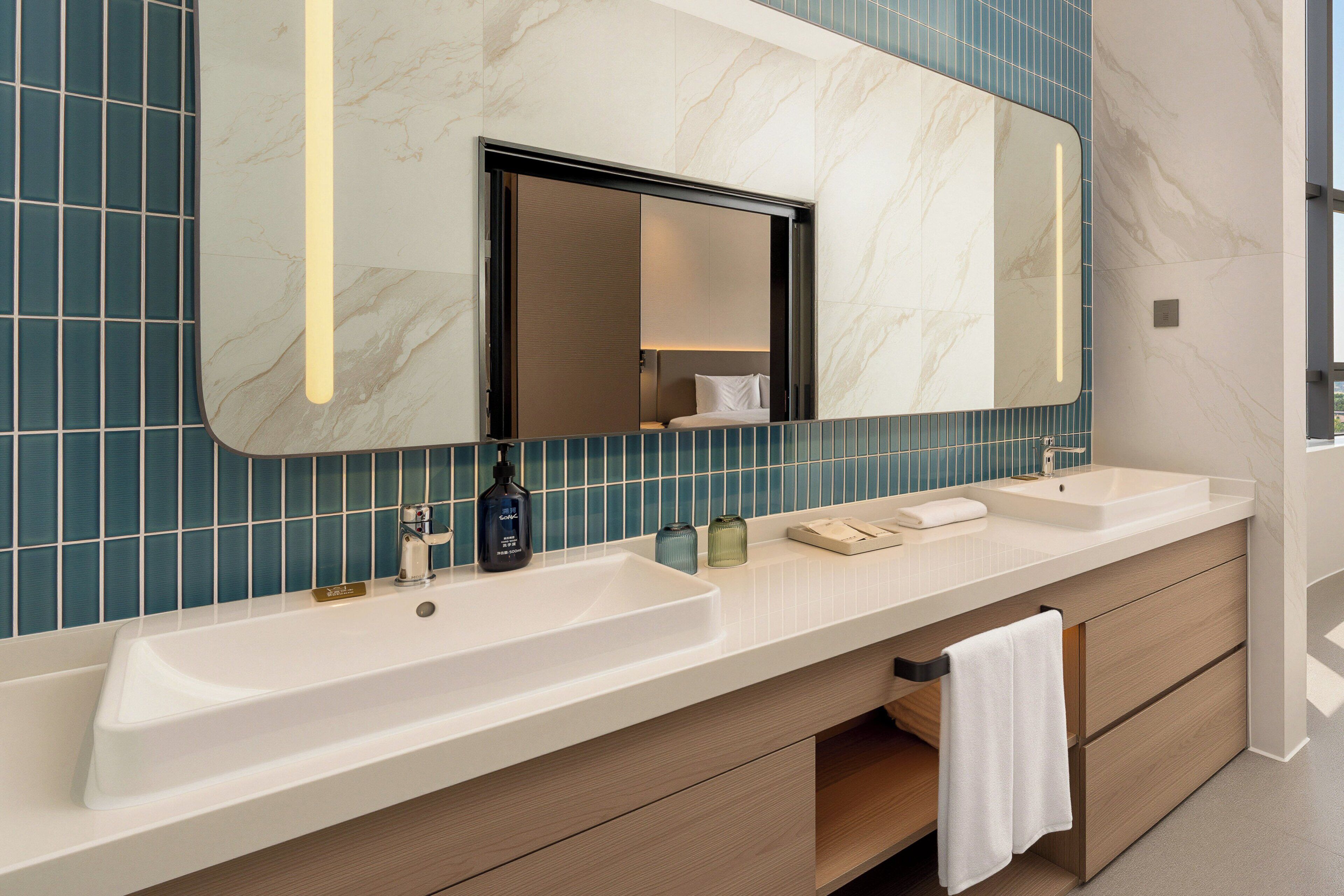 A modern bathroom with a large mirror, two sinks, and a towel rack.