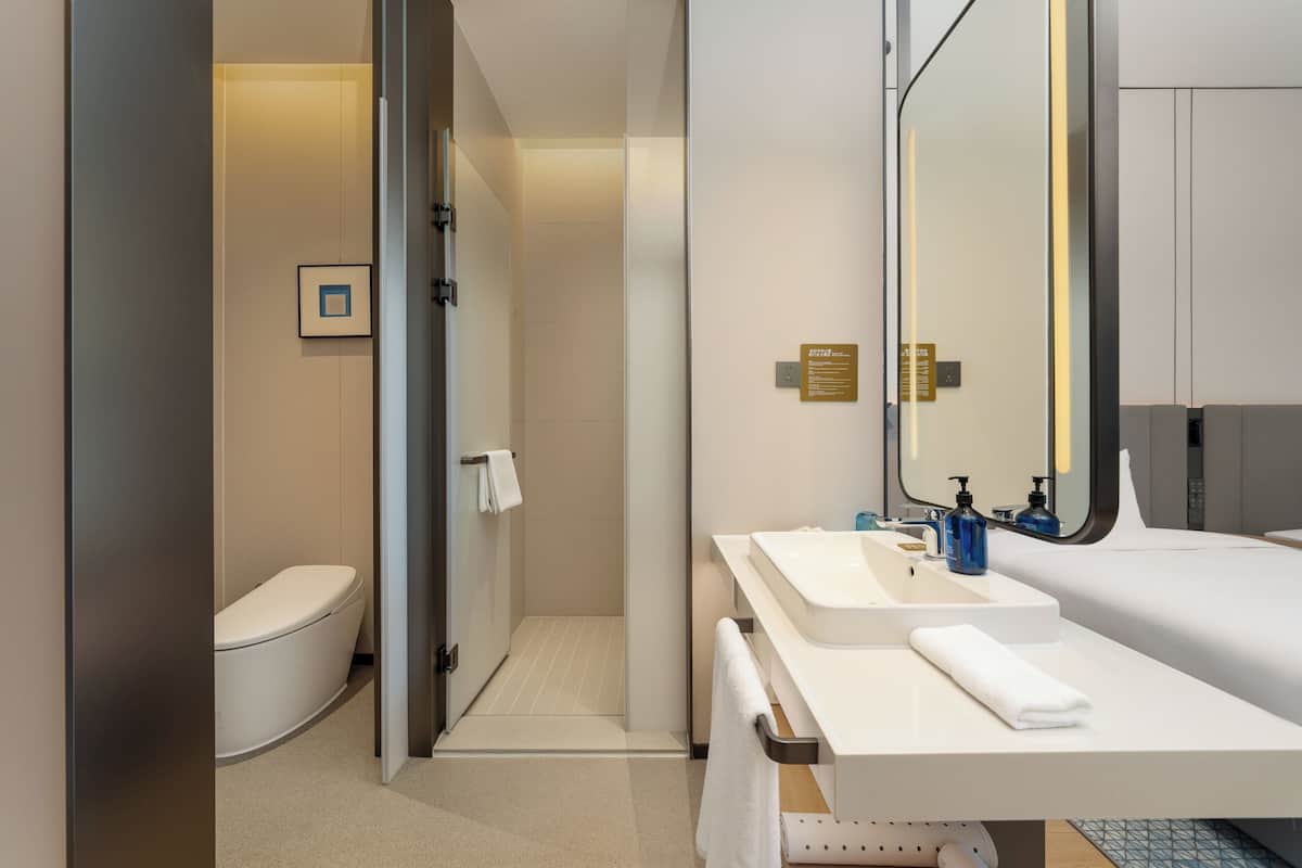 A modern bathroom with a toilet, shower, sink, and mirror.