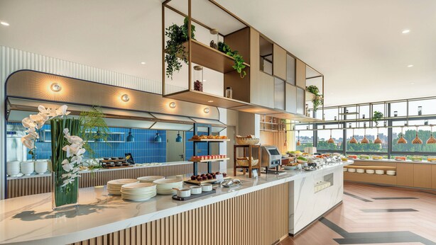 Une cuisine d’hôtel moderne, dotée d’un buffet, de lambris en bois et de grandes fenêtres offrant une vue sur la ville.
