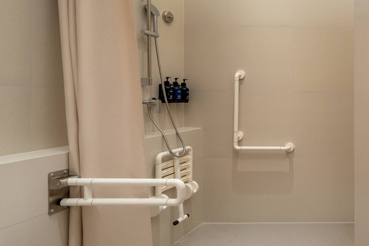 A bathroom with a shower, grab bars, and a towel rack.