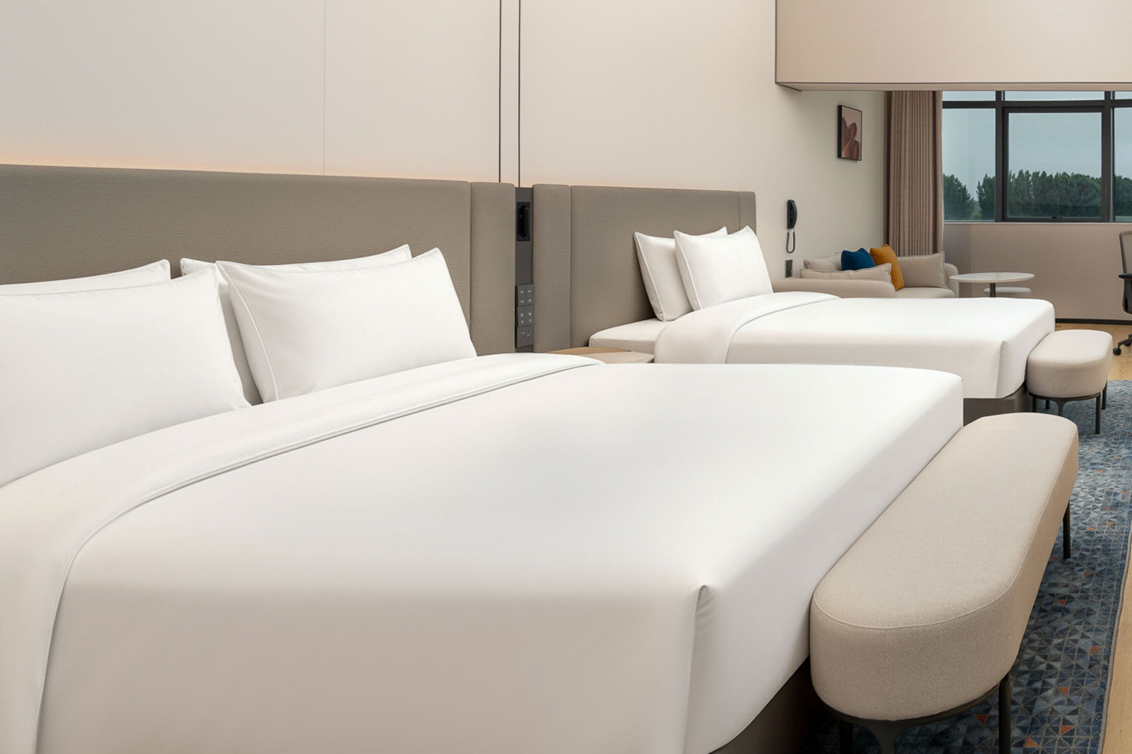 A hotel room with two beds, a sofa, a small table, and a window with a view.