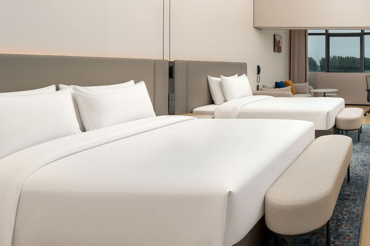 A hotel room with two beds, a sofa, a small table, and a window with a view.