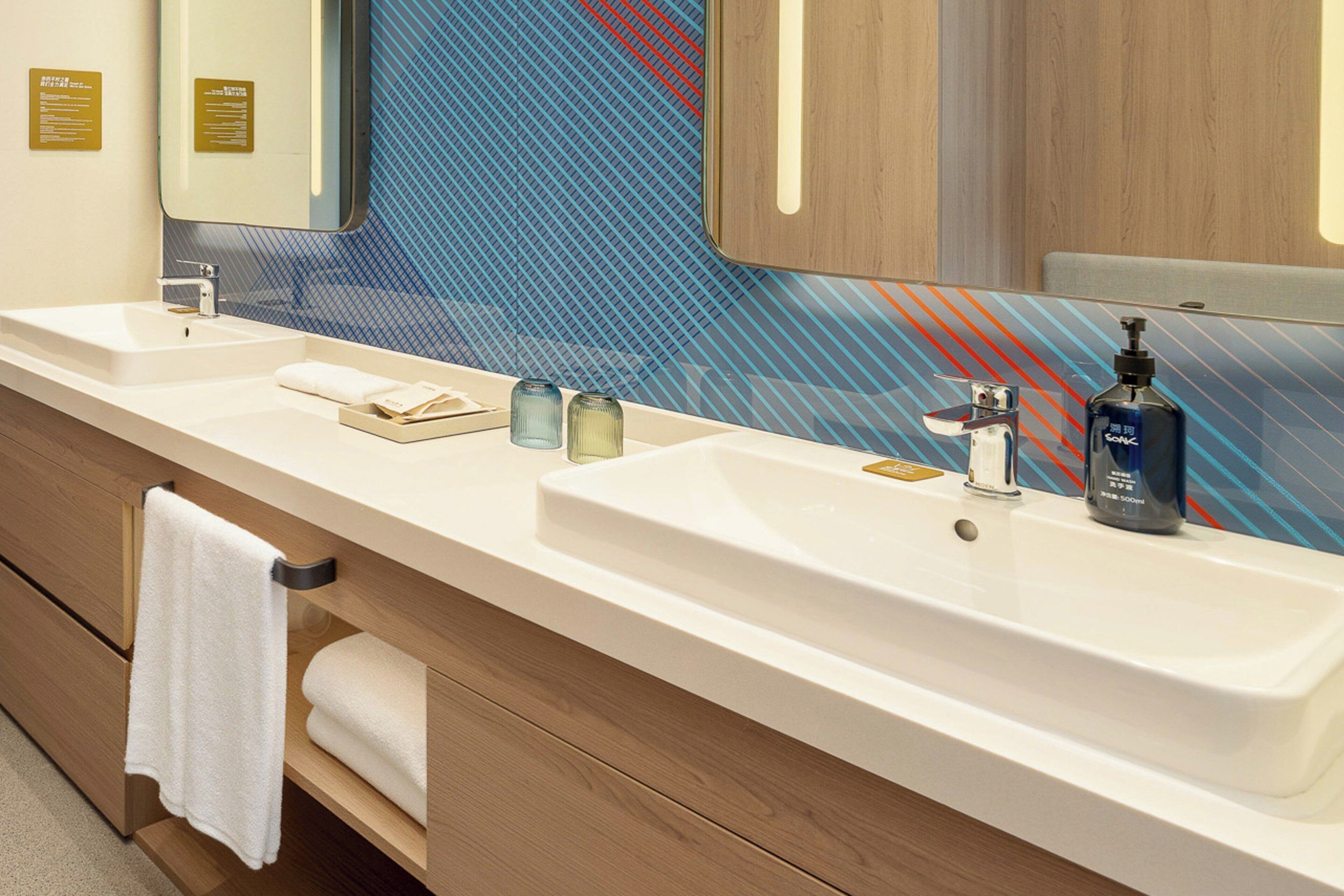 A modern bathroom with two sinks, a large mirror, and a towel rack.