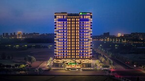 Un hôtel à plusieurs étages, doté d’une entrée imposante, entouré d’un espace paysager et bordé par une route.