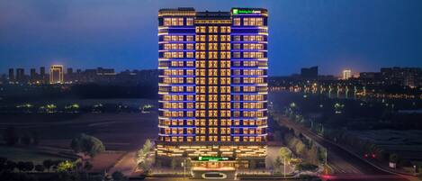 A multi-story hotel with a prominent entrance, surrounded by a landscaped area and a road.