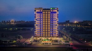 A multi-story hotel with a prominent entrance, surrounded by a landscaped area and a road. - Holiday Inn Express Xinxiang Pingyuan New Area By Ihg (Xinxiang)
