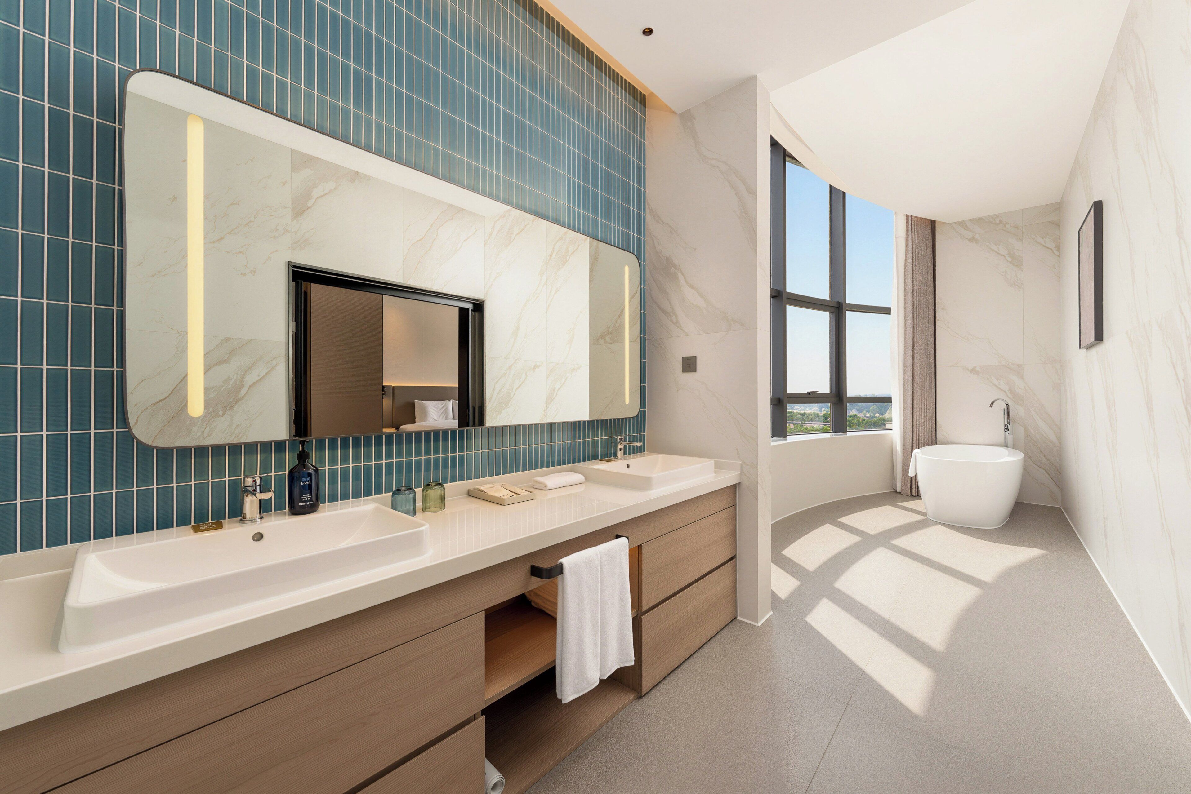 Un baño moderno con un espejo grande, dos lavamanos, una bañera y vistas amplias a través de un ventanal.