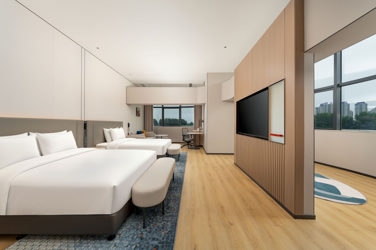 A modern hotel room with a large bed, a desk, a TV, and a city view.