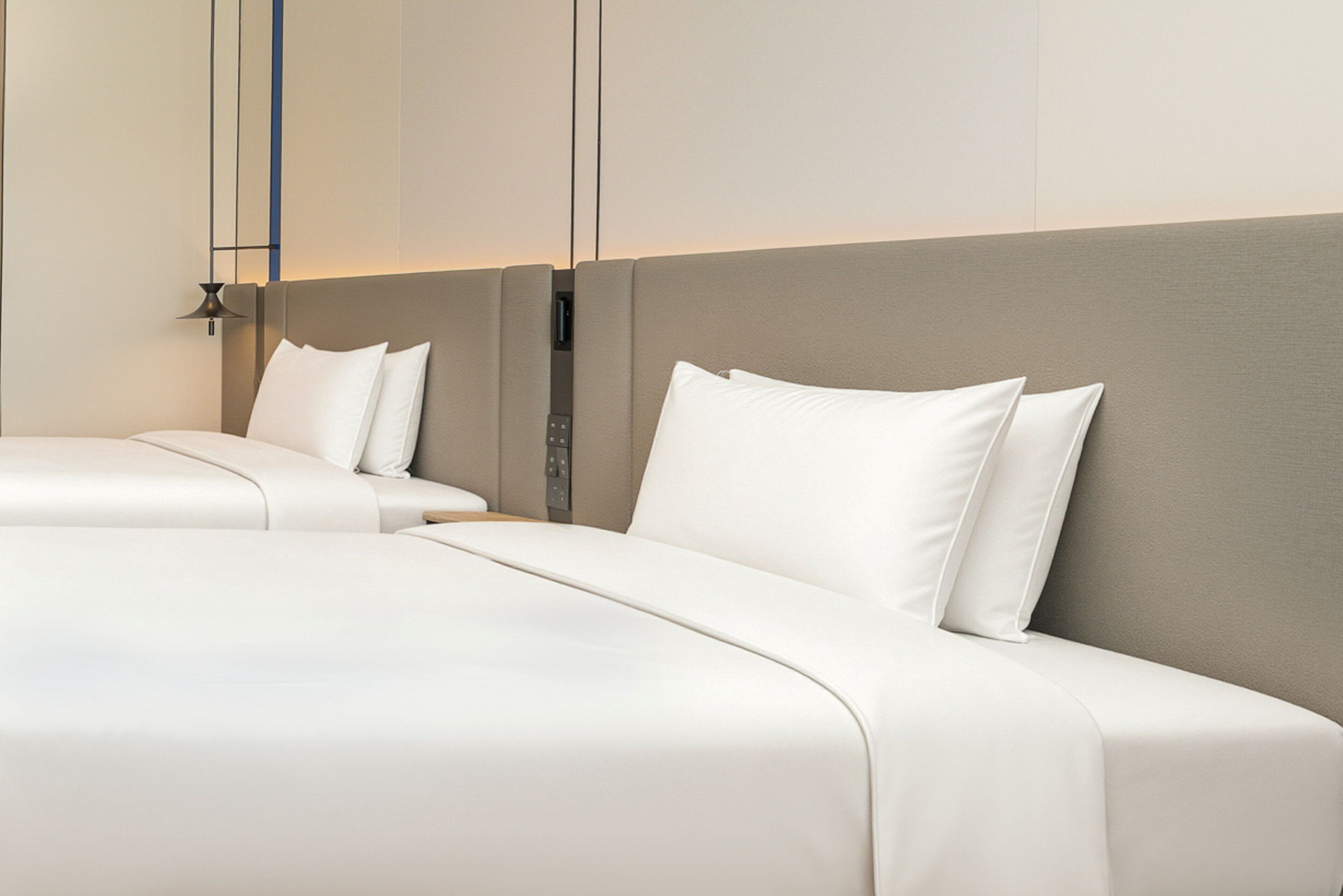 A hotel room with two beds, a headboard, and a wall-mounted control panel.