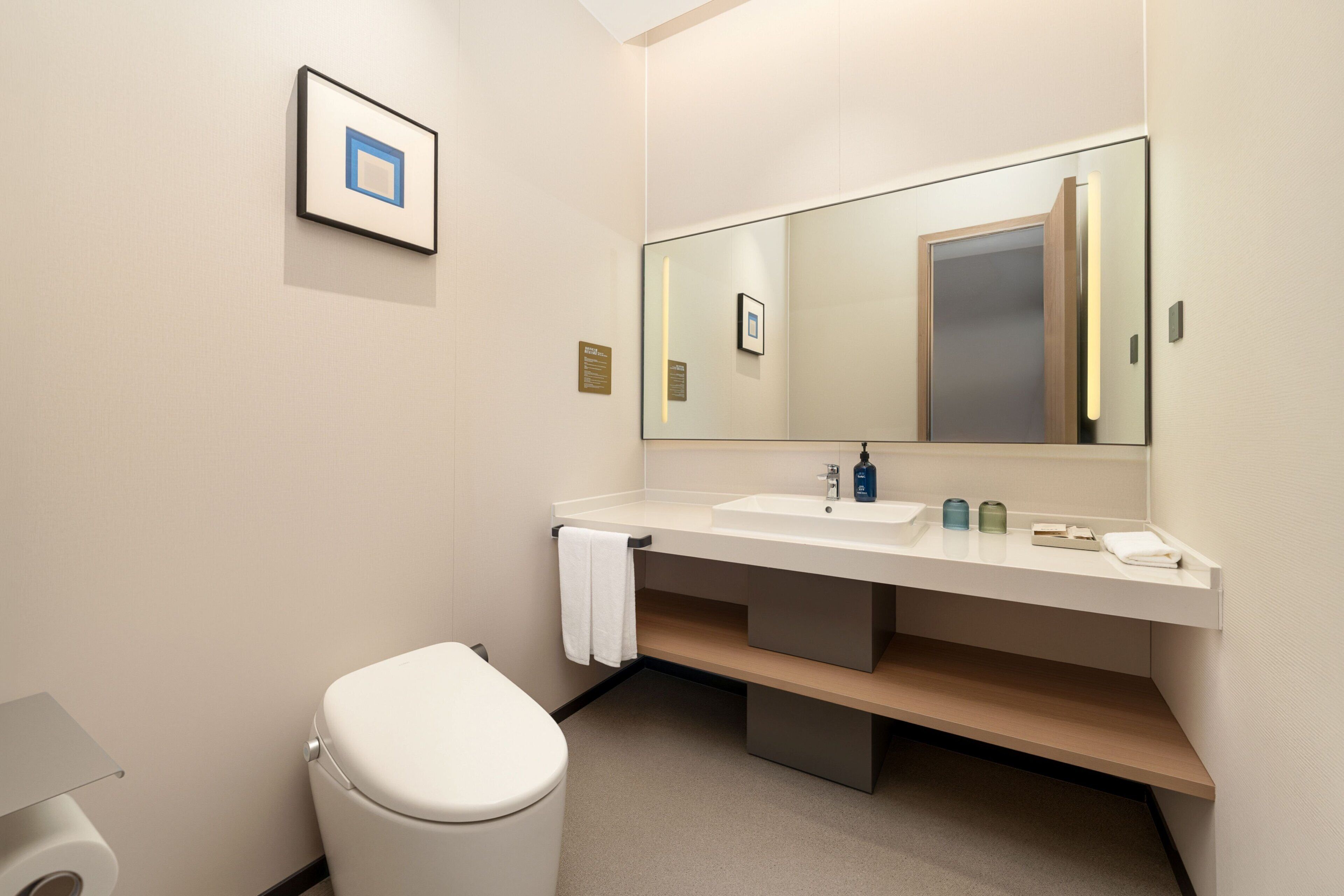 Un baño moderno con inodoro, lavabo, espejo y un cuadro en la pared.