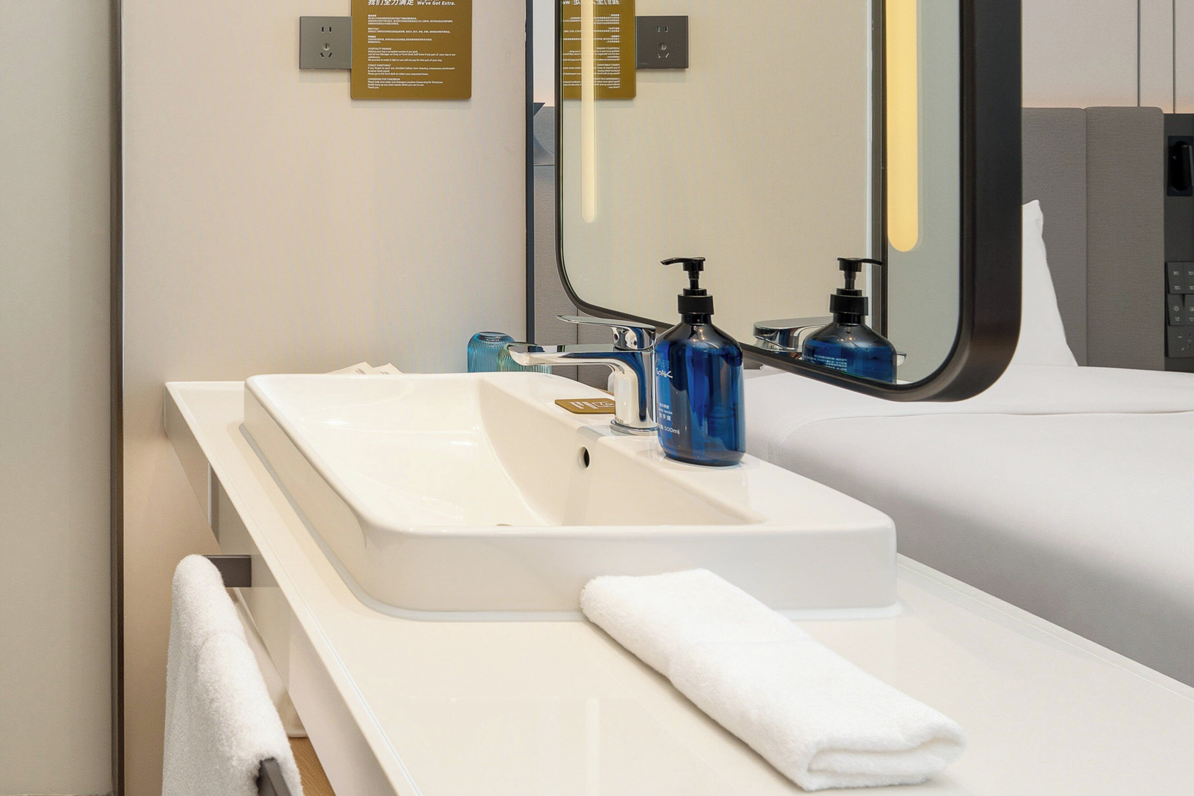 A modern bathroom with a white sink, a mirror, a towel, and a soap dispenser.