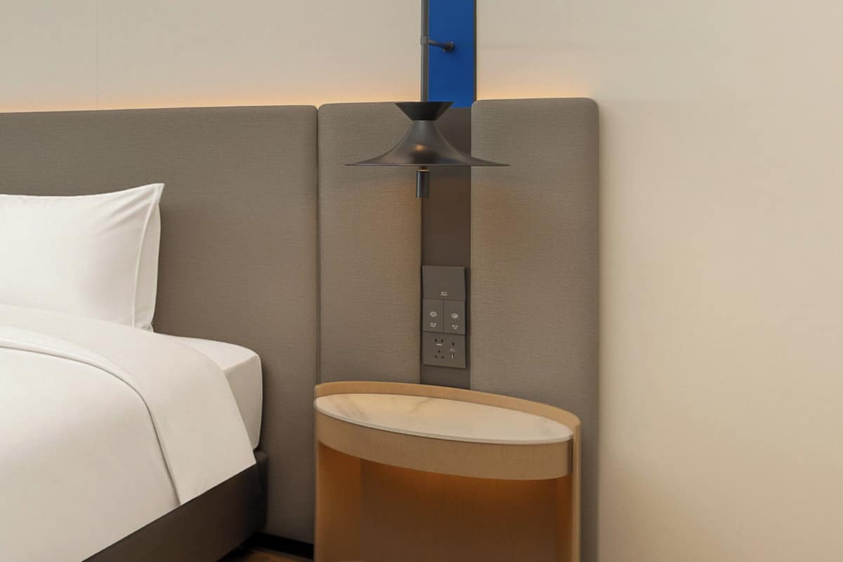 A hotel room with a bed, a nightstand, a lamp, and a wall-mounted control panel.