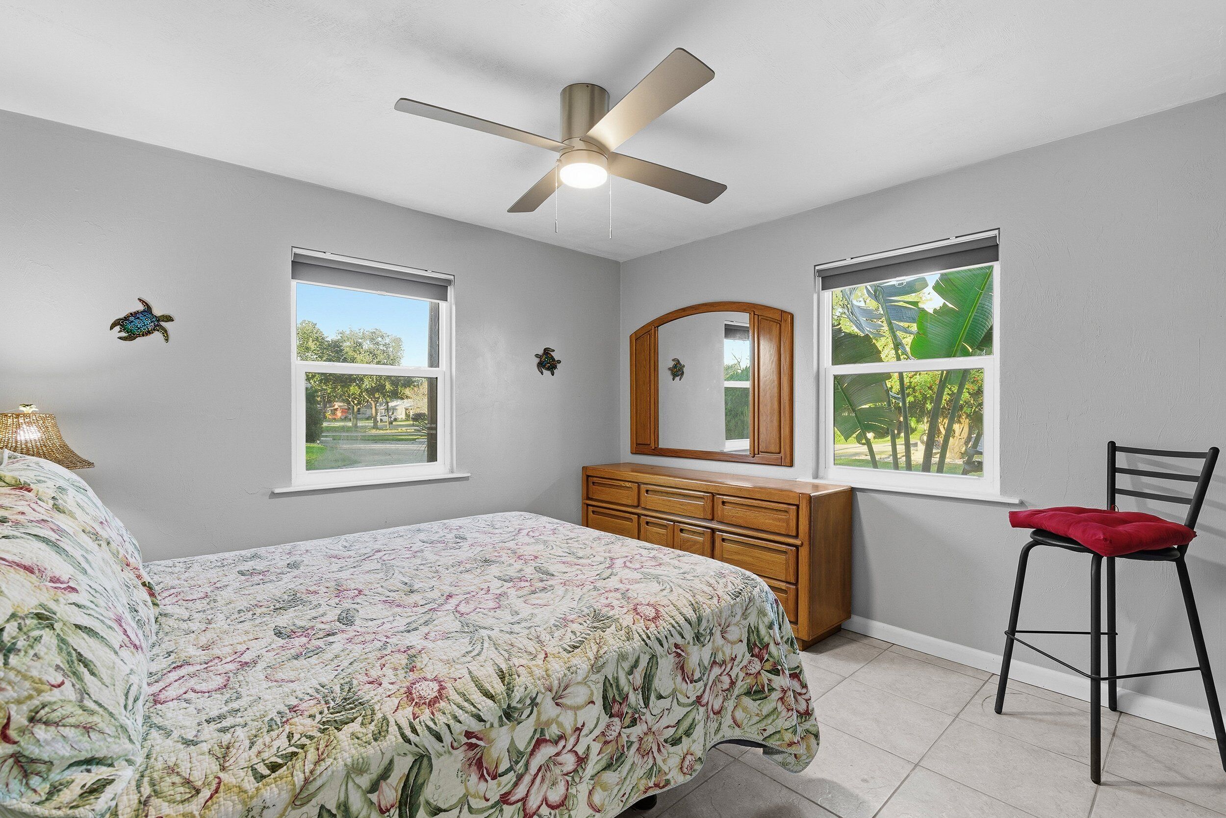 A bedroom with a bed, a dresser, a chair, a ceiling fan, and two windows.
