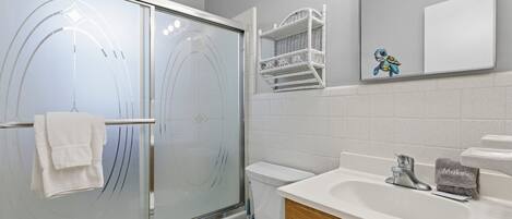 Et badeværelse med glasbrusekabine, toilet, håndvask med håndklæde og spejl.