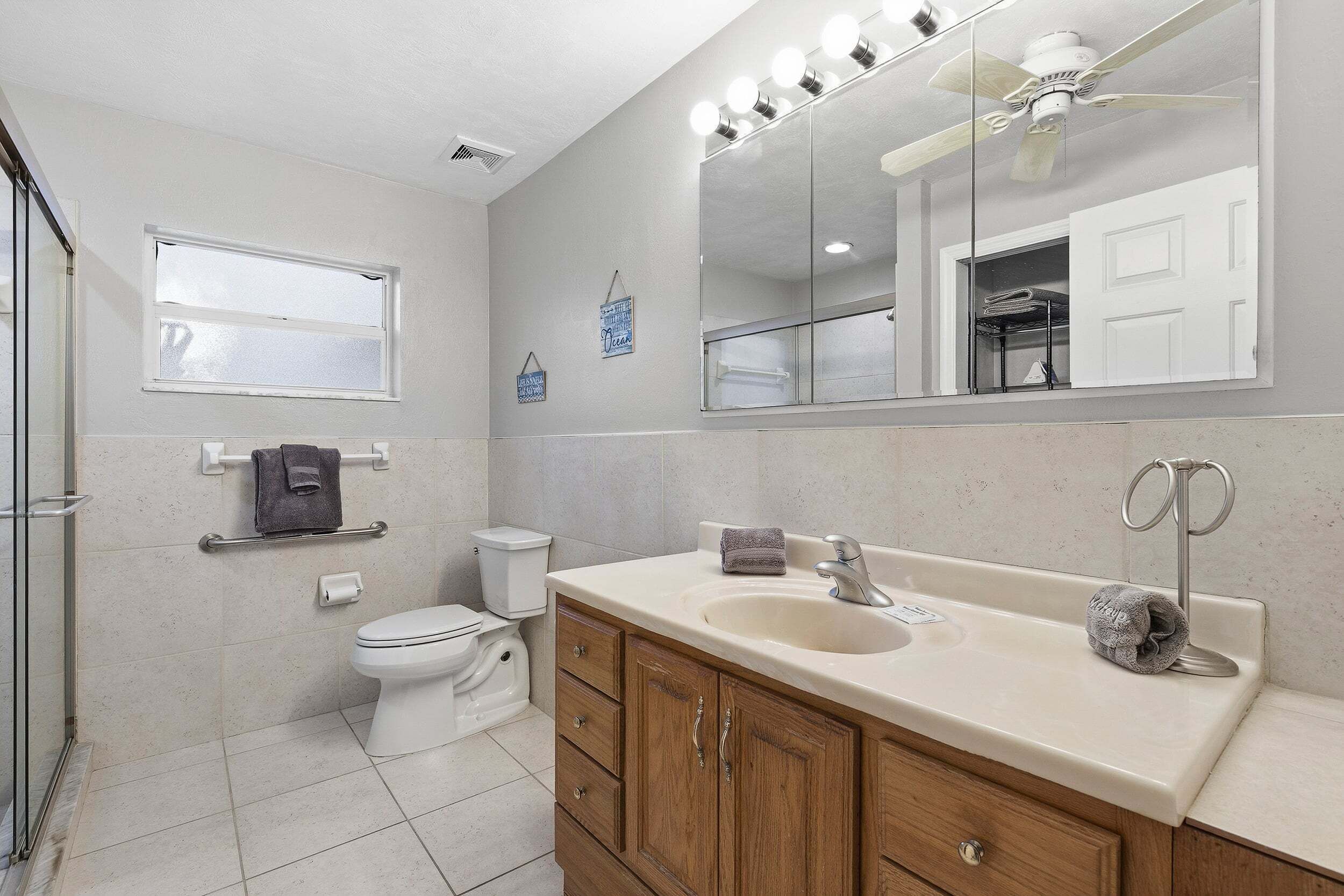 A bathroom with a toilet, sink, vanity, and a mirror with lights.