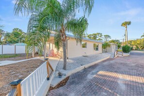 A residential property with a paved driveway, a small garden area with a palm tree, and a white fence. - Sun and Fun (Port Orange)