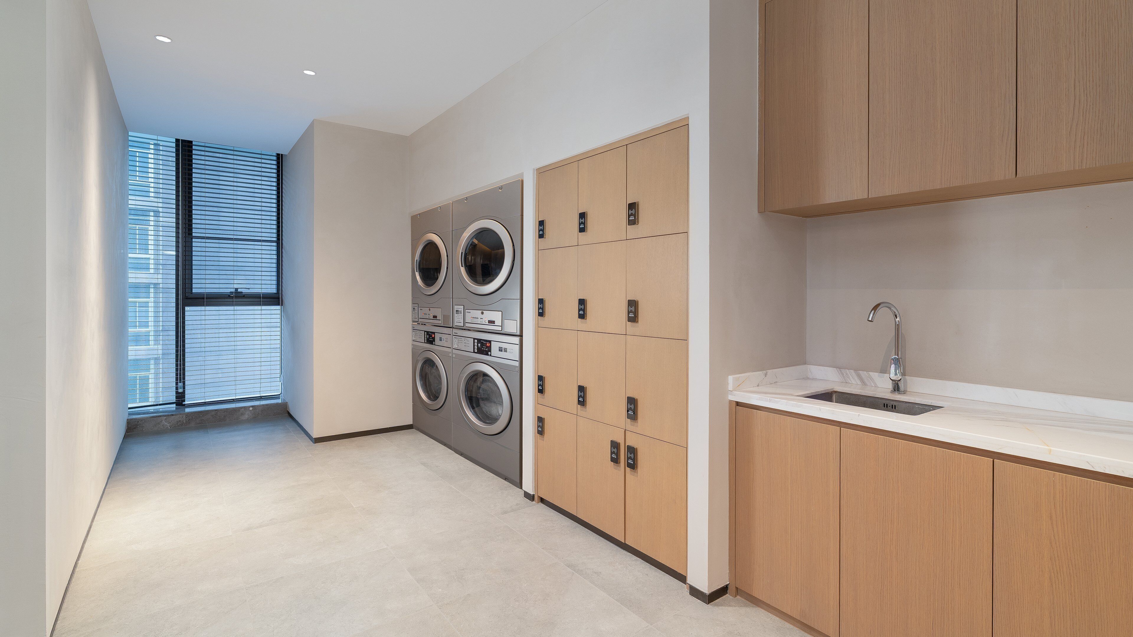 A modern laundry room with a large washing machine and dryer, a sink, and a view of the outside through a window.