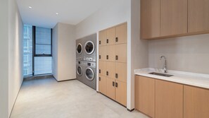 A modern laundry room with a large washing machine and dryer, a sink, and a view of the outside through a window. - Even Hotel Xi An High Tech Zone By Ihg (Xi'an)