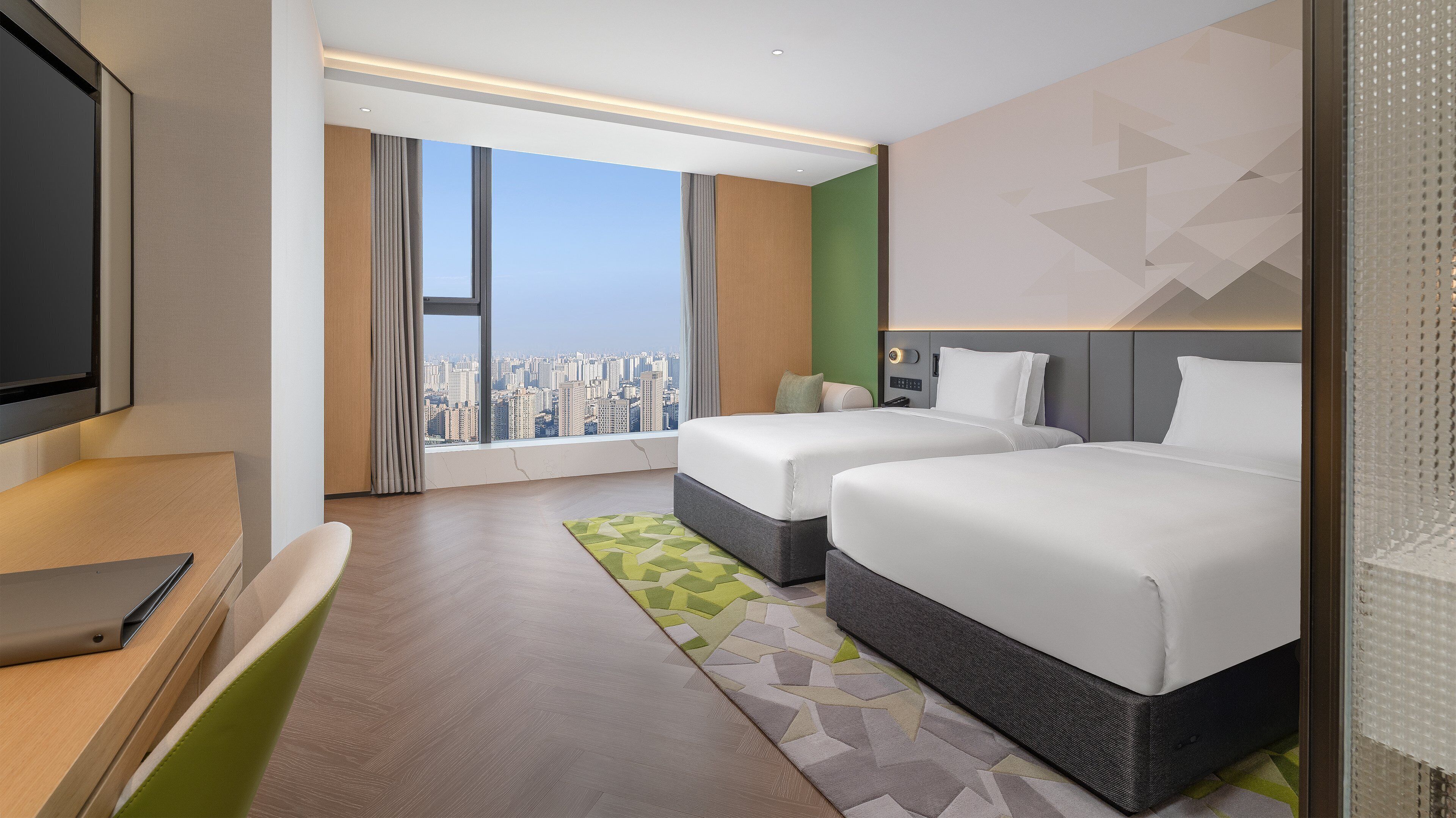 A hotel room with a large window, two beds, a desk, and a television.