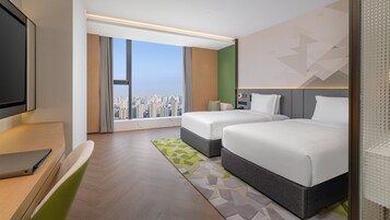 A hotel room with a large window, two beds, a desk, and a television.