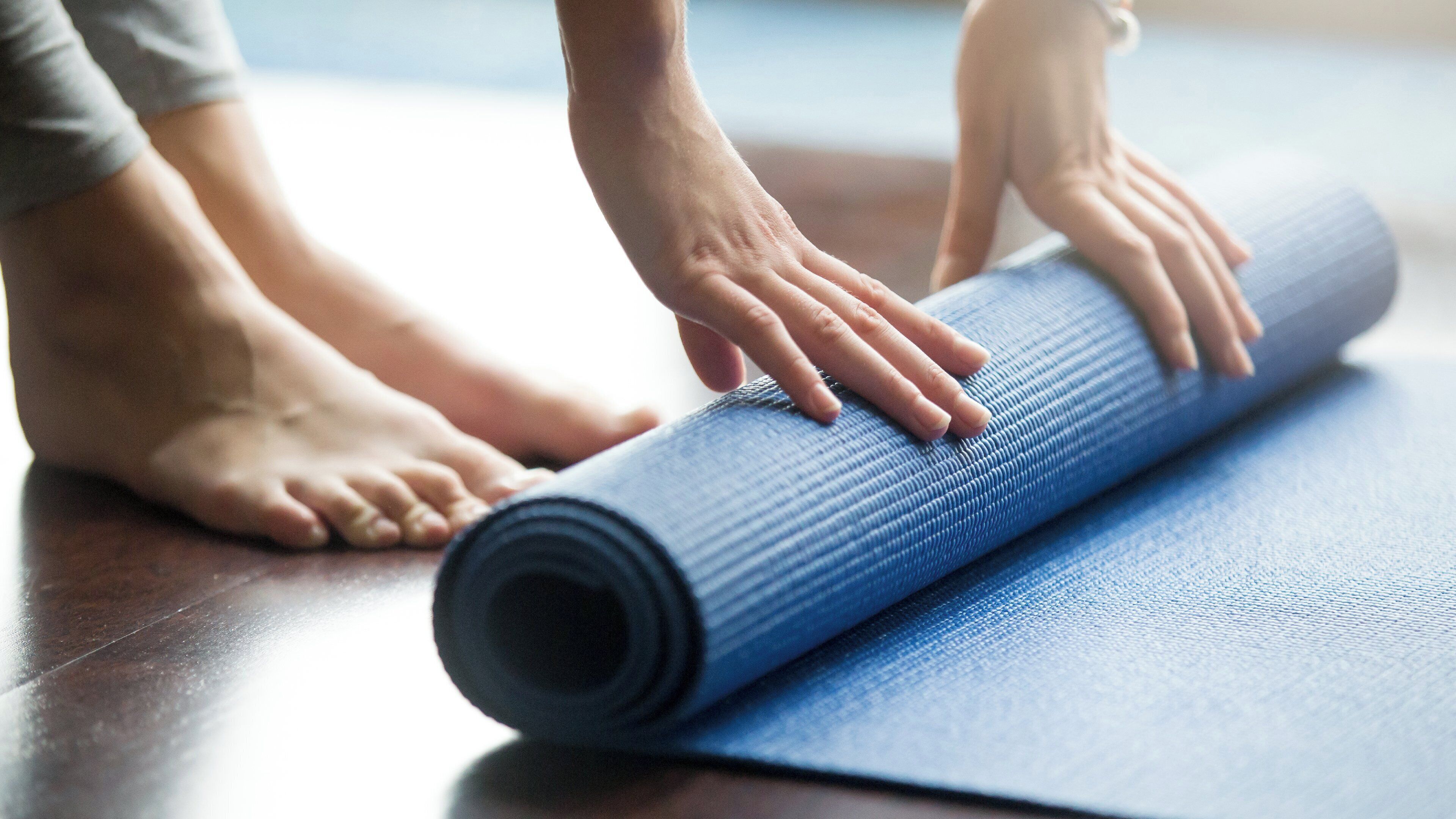 Una persona extendiendo una colchoneta de yoga sobre un piso de madera.