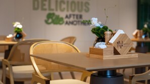 A hotel room with a wooden table, wicker chairs, a wall with a sign reading 'DELICIOUS AFTER ANOTHER', and a small plant on the table. - Even Hotel Xi An High Tech Zone By Ihg (Xi'an)