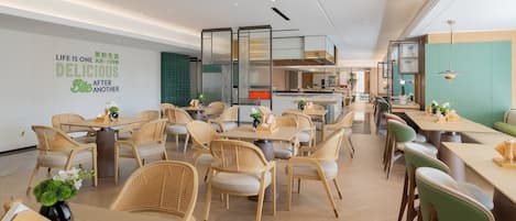 A modern hotel dining area with wicker chairs, wooden tables, and a green-tiled wall.