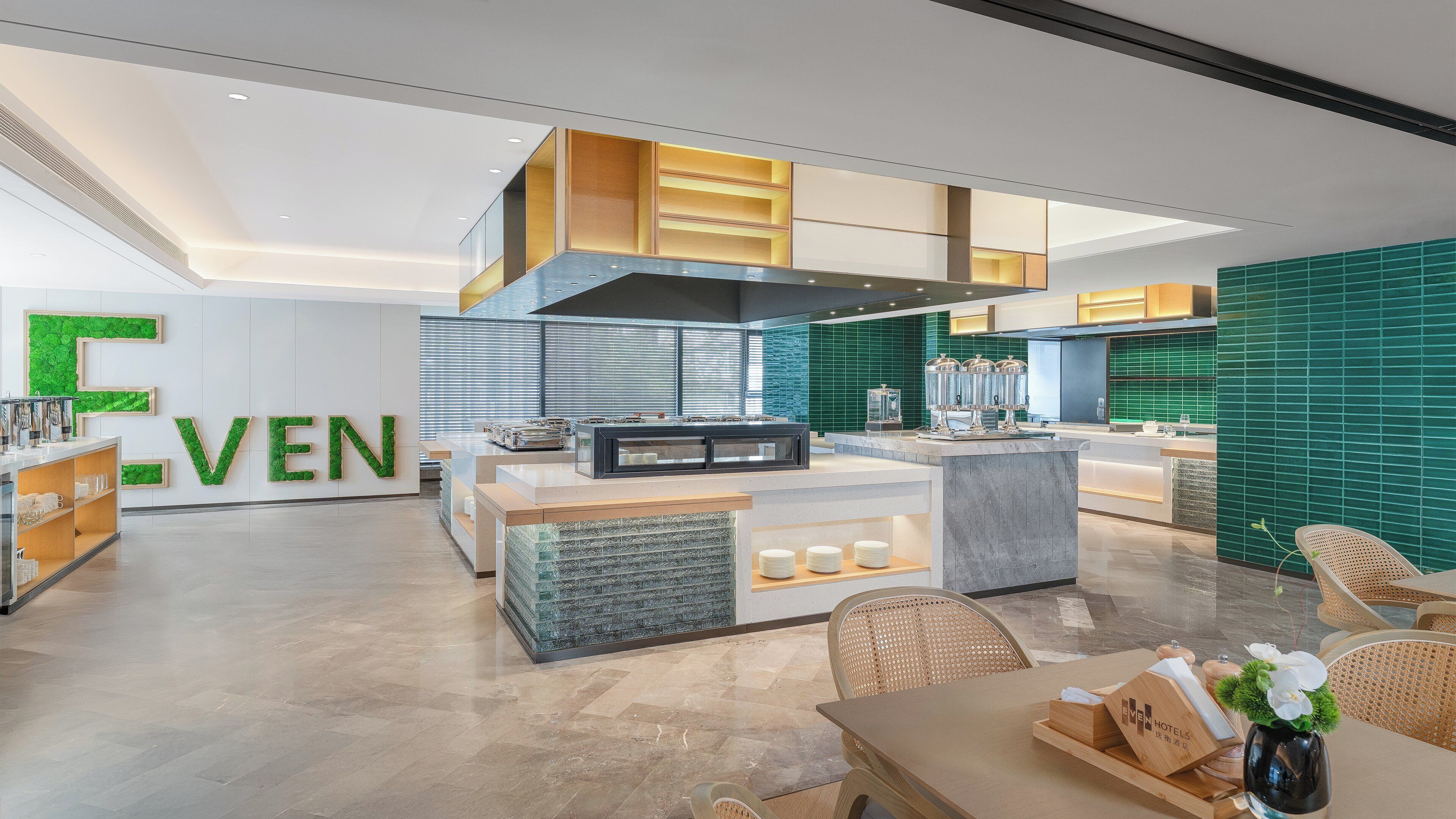 A modern hotel lobby with a central island, seating area, and a large 'EVEN' sign on the wall.