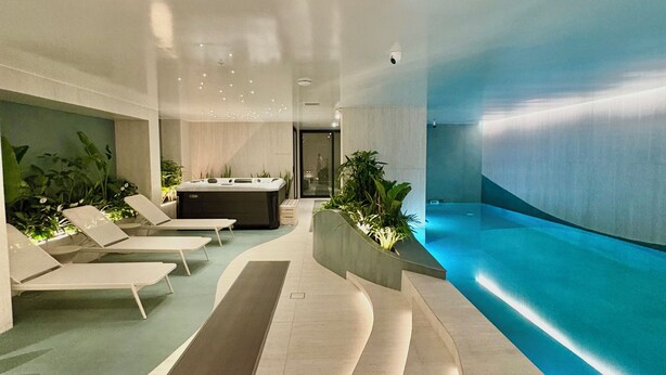 Un área interior de piscina moderna con sillones de descanso, un espacio central para sentarse y una fuente de agua iluminada en azul.