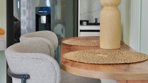 Una cocina moderna con refrigerador, un florero de madera con plantas secas y una mesa redonda de madera con un mantel tejido.