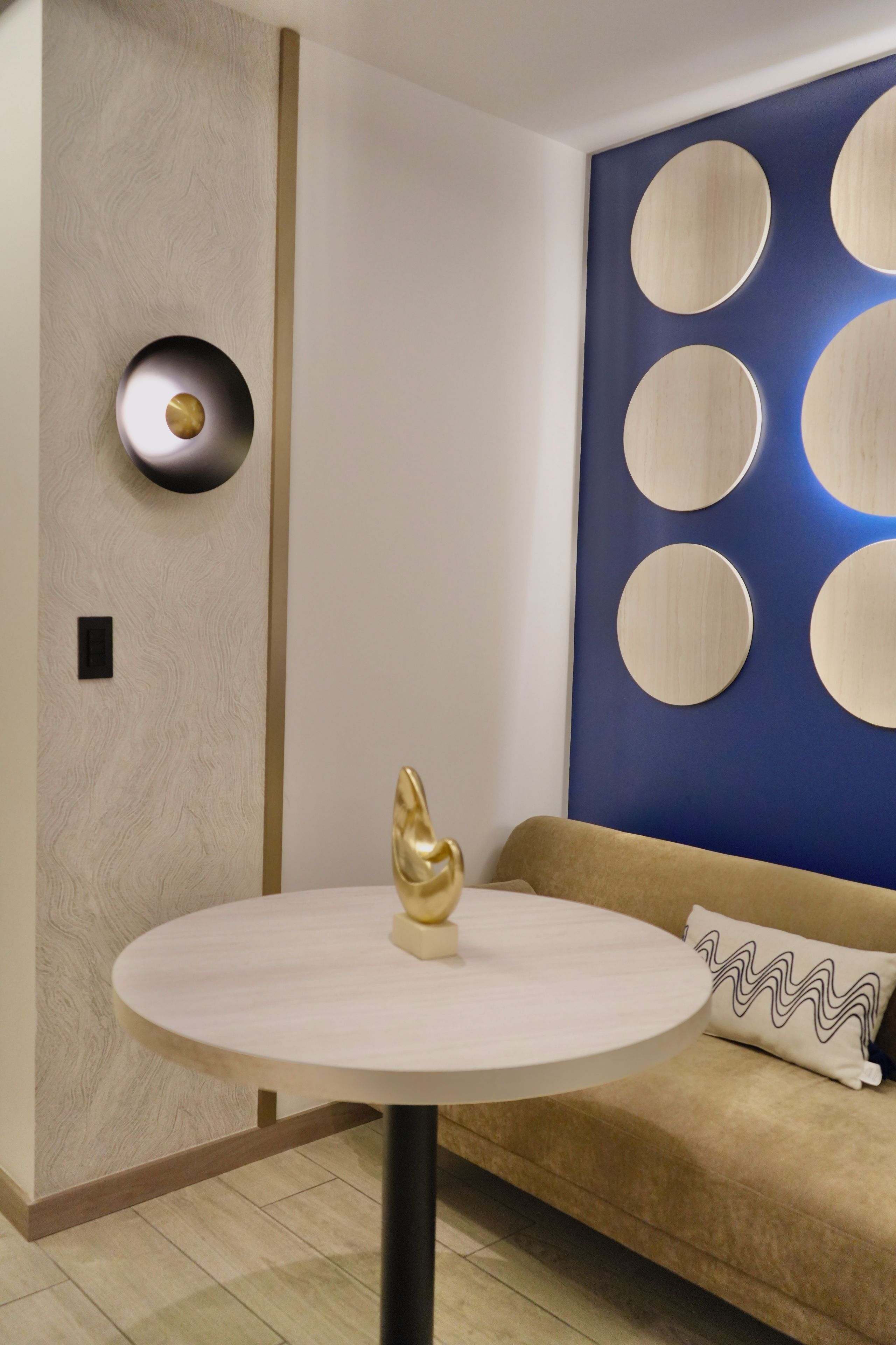 A modern interior with a round table, a decorative golden sculpture, a wall with circular patterns, and a sofa with a patterned pillow.