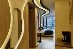 A modern hotel room with a curved wall design, a bed with a dark cover, a small round table, and a coffee machine. - Cielo Residences by Nomad-in (Quito)