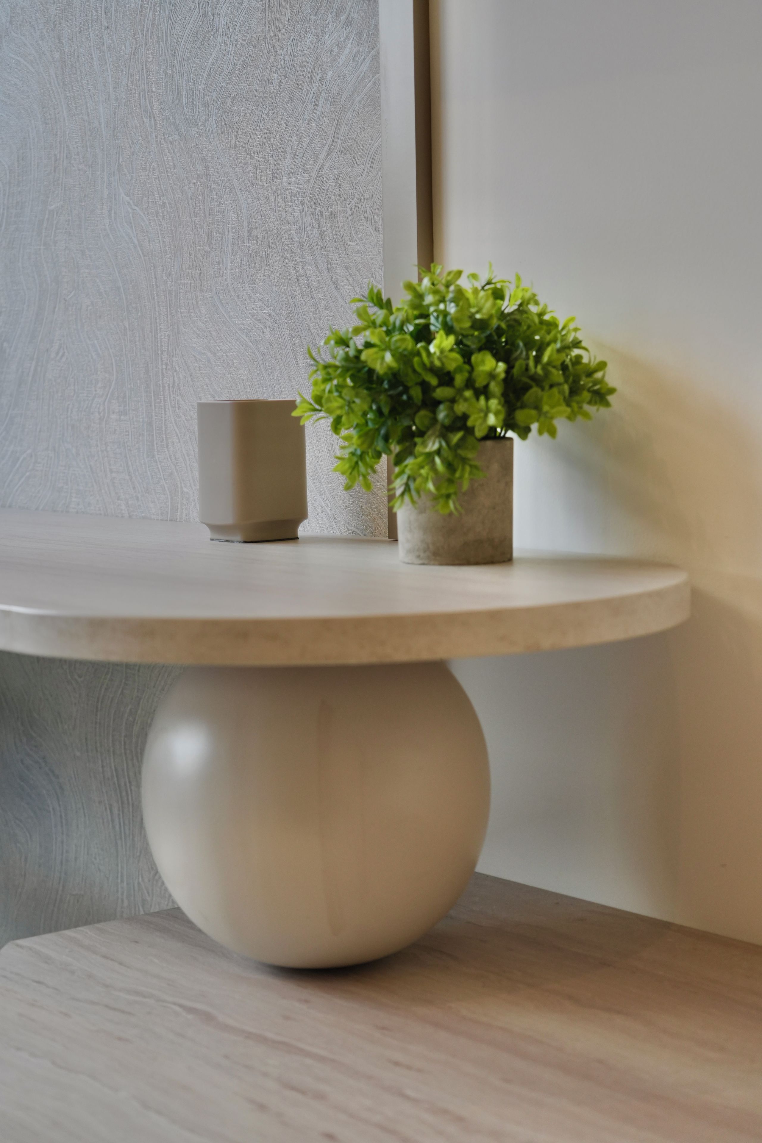 A round table with a beige base and a potted plant with green leaves.