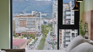 Habitación de hotel con cama, vista a la ciudad y ventana con montaña al fondo.