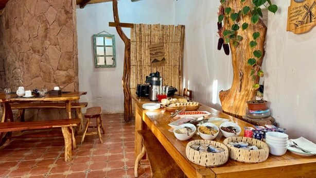 Un coin repas rustique avec une longue table en bois dressée pour le repas, entouré de murs en pierre et agrémenté d’un décor en bambou.