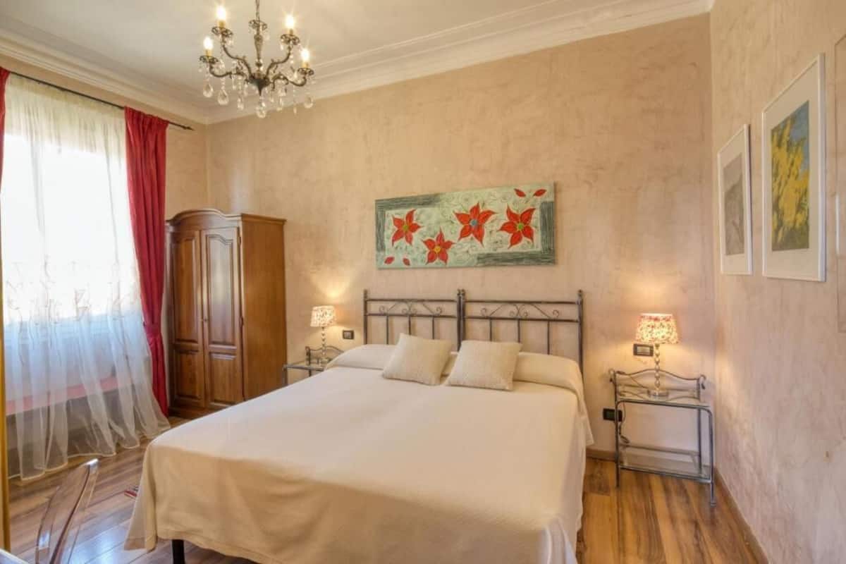 A bedroom with a large bed, a chandelier, a wooden wardrobe, and a painting on the wall.
