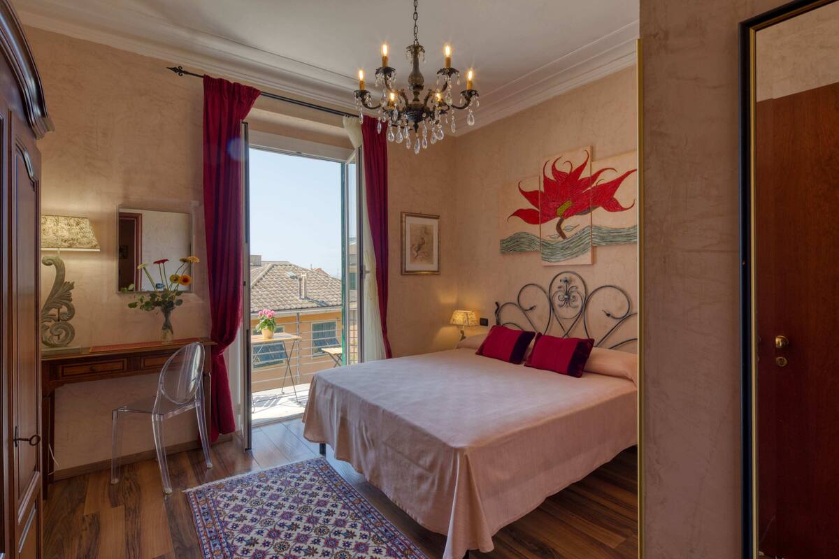 A bedroom with a bed, a chandelier, a desk with a chair, and a window with curtains.