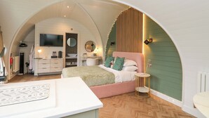A bedroom with a pink bed, a white desk, a TV, and a green accent wall. - Crofters Suite (Acharacle)