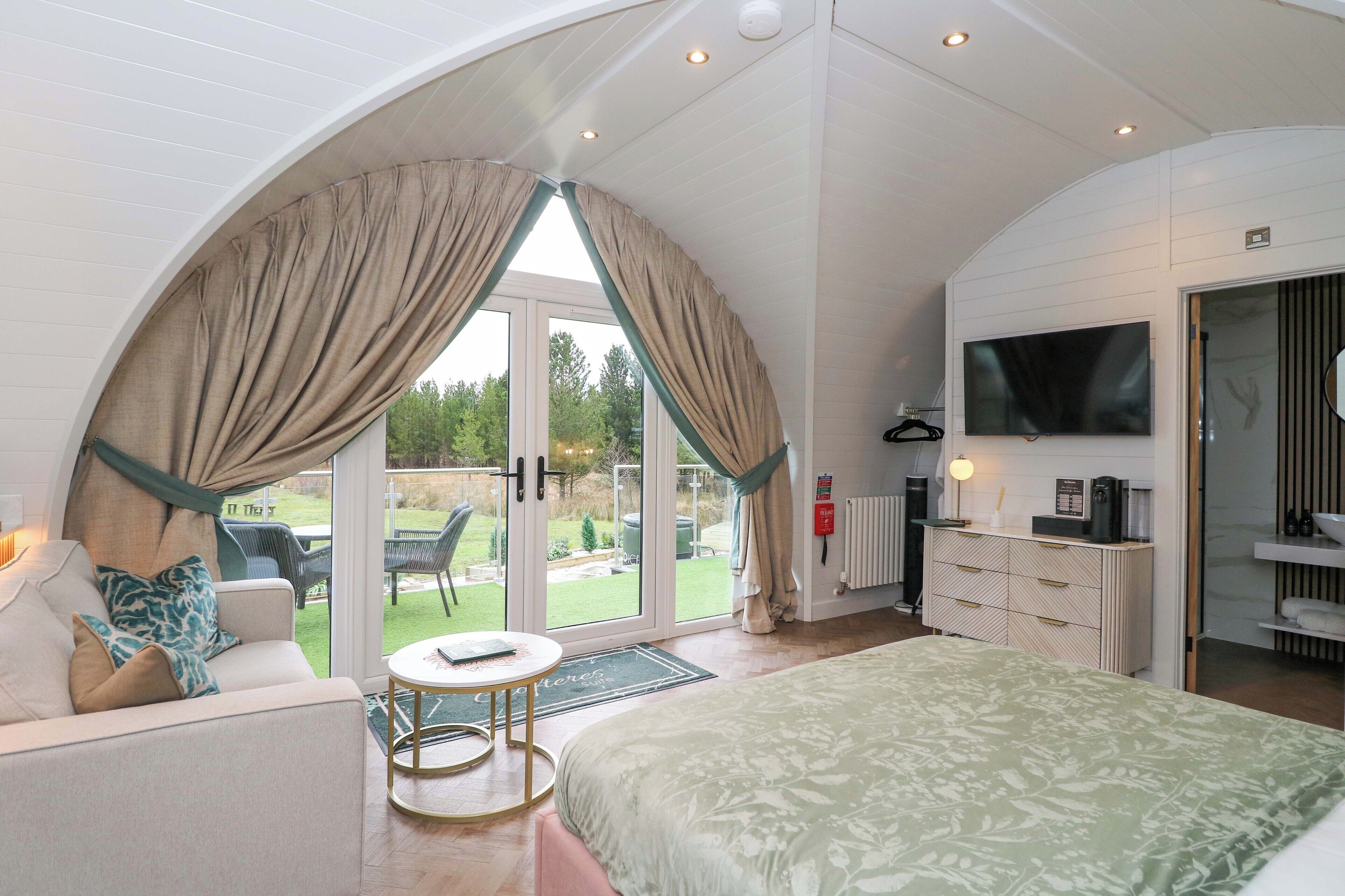 A bedroom with a large bed, a TV, a desk, and a view of the outdoors.