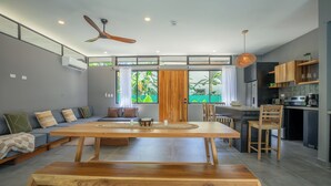 Una cucina moderna con zona pranzo, caratterizzata da un tavolo e sedie in legno, una ventola a soffitto e vista sul verde circostante.