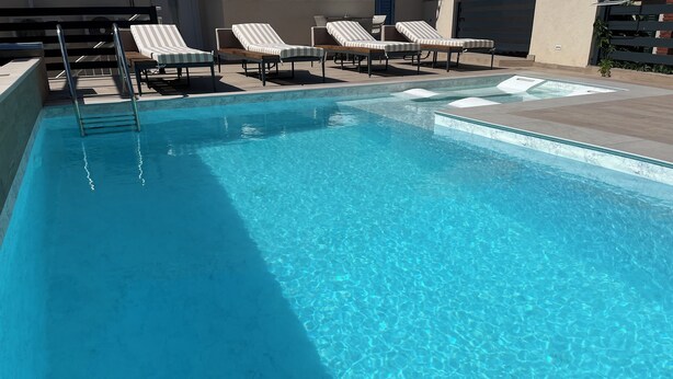 Una piscina trasparente con sedie a sdraio e una scala.