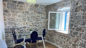 Una stanza con pareti in pietra, un tavolo da pranzo con sedie, una finestra e un divano con cuscini decorati.